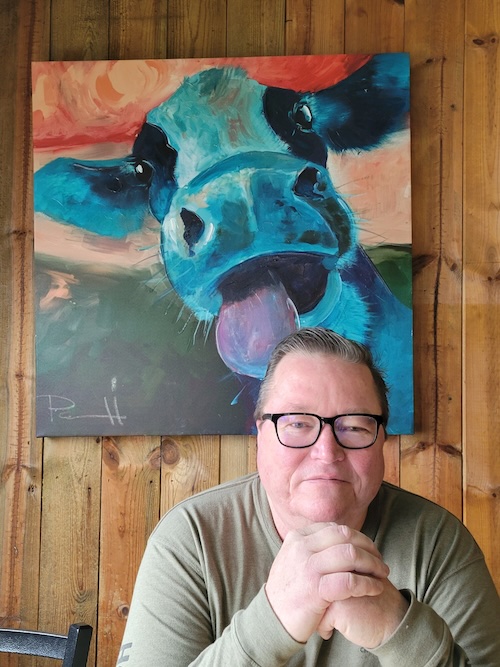 I'm sitting in front of a painting of a cow that appears to be licking the top of my head.
